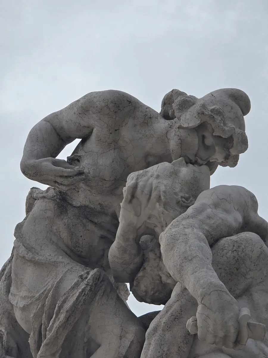 Escultura de mármol de dos figuras en un beso, contra un cielo gris